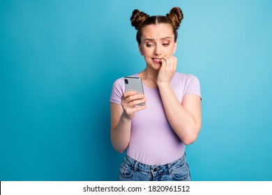 Photo of attractive pretty teen lady biting fingers two buns influencer hold telephone reading bad news comments unfollows wear casual purple t-shirt isolated blue color background