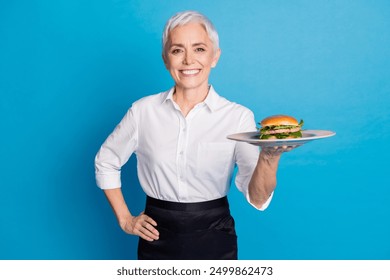 Photo of attractive senior woman small business cafe owner serve burger tray dressed waitress uniform isolated on blue color background - Powered by Shutterstock