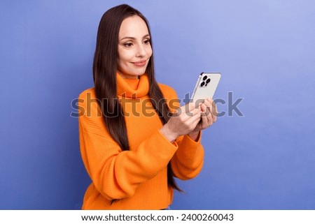 Photo of attractive young happy woman in orange pullover browsing cellphone check spam sms in gmail isolated on violet color background