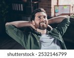 Photo of attractive young man relax hands behind head wear green shirt comfortable modern office loft room interior indoors workspace