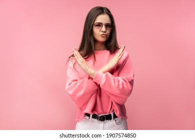 Photo of attractive young woman in glasses, not allow to do something, dislike and disagree. Wears casual pink t-shirt white pants isolated pink color background