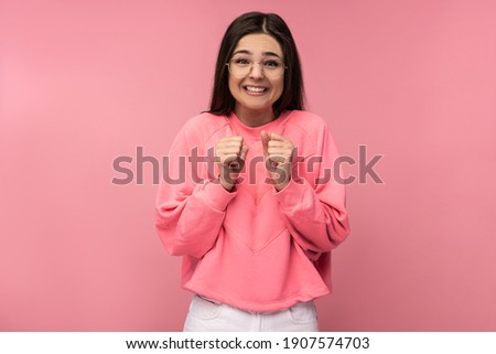 Photo of attractive young woman in glasses waits impatiently, looks forward. Wears casual pink t-shirt isolated pink color background