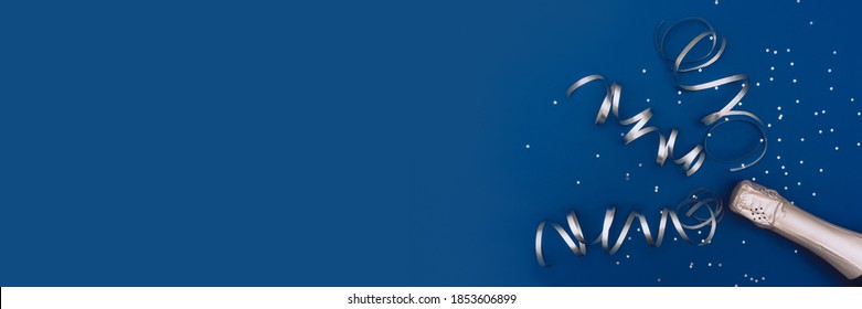 Photo banner of champagne bottle with confetti stars and party streamers on trendy classic blue background. Christmas, birthday or wedding concept. Flat lay, top view, copy space, mock-up. - Powered by Shutterstock