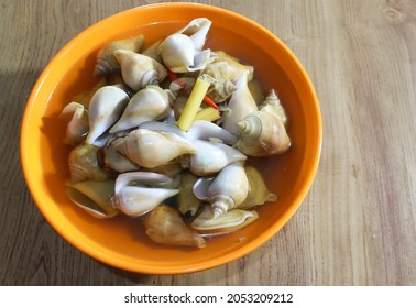 Photo of Batam's Indonesian seafood menu Snail GONG GONG boiled in an orange bowl on a wooden table