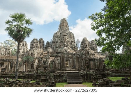 A photo of the Bayon Temple taken from the north entrance. The carvings of serene faces are visible on the sandstone towers and a seated statue can be seen through the main doorway. 
