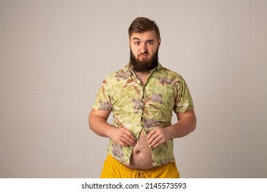 Photo Of A Bearded Man In A Summer Hawaiian Shirt. A Young Man Tries To Fasten The Buttons On His Shirt. A Fat Belly Makes It Difficult To Button Up A Sweatshirt