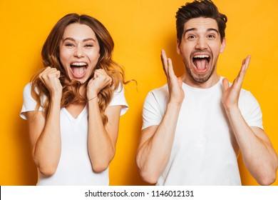 Photo of beautiful admired couple man and woman in basic clothing screaming in surprise or delight and touching cheeks isolated over yellow background