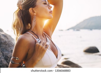 Photo of beautiful boho styled model wearing white swimsuit and silver bohemian jewelery on the beach in sunset