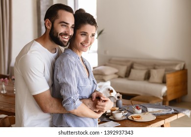 Foto von einem wunderschönen Brünettenpaar in verliebten Mann und Frau 20er lächelnd während sie zusammen in Wohnung umarmten