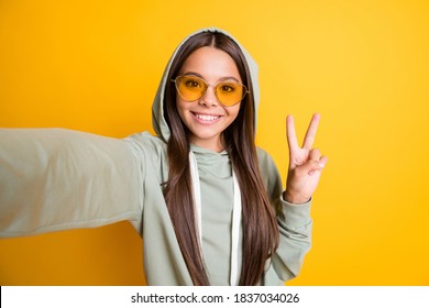 Photo of beautiful brunette hair kid show arm finger v-sign on selfie hoodie isolated on yellow color background