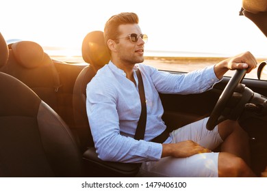 Photo Of Beautiful Caucasian Man Wearing Sunglasses Driving Convertible Car By Seaside At Sunrise