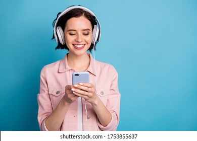 Photo Of Beautiful Cheerful Lady Hold Telephone Browsing Listen Modern Technology Headphones Enjoy Music Send Song Friends Wear Casual Pink Jacket Pants Isolated Blue Color Background