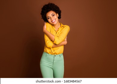 Photo of beautiful cute dark skin lady holding shoulders enjoy own private company love herself wear yellow shirt green trousers isolated brown color background
