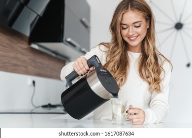Photo of beautiful happy woman with blonde hair smiling and making tea while standing at cozy kitchen - Powered by Shutterstock