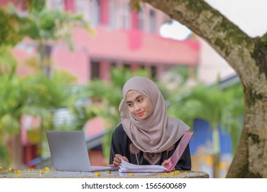 Photo Of  Beautiful Islamic Female Student Wearing Headscarf Sitting Under The Tree  And Using Silver Laptop.