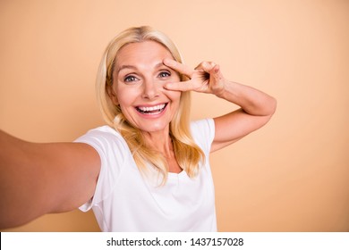 Photo of beautiful lady make selfies v-sign symbol near eye say hi hello wear white casual t-shirt isolated pastel beige background