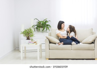 Photo of beautiful mother hugging with her cute little daughter and look each other in living room.