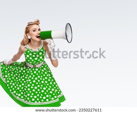 Photo of beautiful pinup woman hold mega phone, shout, saying advertise. Happy girl in green pin up dress with megaphone loudspeaker. Isolated grey background. Big sales ad concept image.