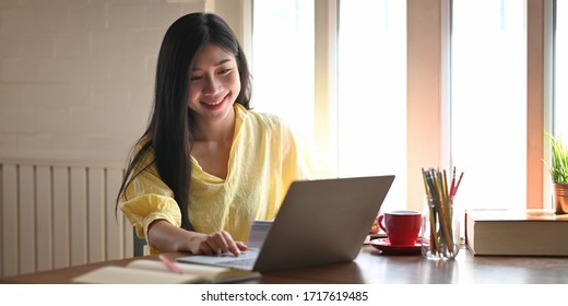 Photo of beautiful woman relaxing and using a computer laptop while sitting at the wooden working desk over comfortable living room windows as background. Student tutoring and online learning concept. - Shutterstock ID 1717619485