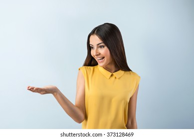 Photo of beautiful young business woman standing near gray background. Smiling woman with yellow shirt looking and pointing aside - Shutterstock ID 373128469