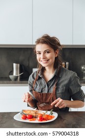 Photo of beautiful young lady sitting in kitchen while eating fish and tomatoes. - Shutterstock ID 579004318