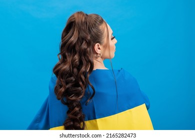 Photo From Behind Of A Woman With Long Curly Hair Tied In A Ponytail. The Girl Covers Her Back With A Blue And Yellow Flag, Solidarity With Ukraine.