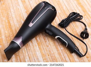 Photo of black blow dryer over wooden surface.