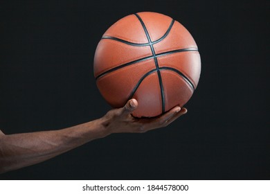 Photo Of A Black Man Hand Holding A Basketball Isolated On Black Background.