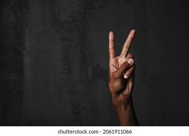 Photo of black man's hand showing peace gesture at camera isolated over dark background