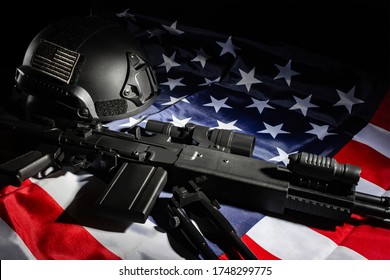 Photo of a black sniper rifle laying on american flag table with soldier helmet with american patch on black background.