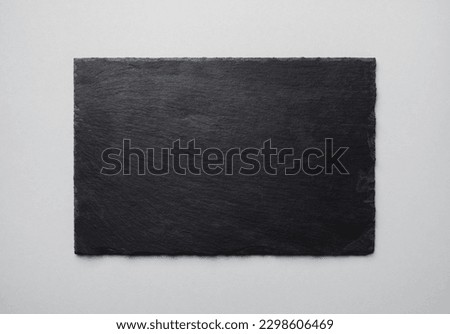 Photo of black stone slate plate on gray paper background. Copy space for text. Flat lay.