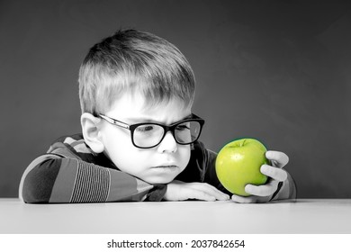 Photo black and white. The boy in glasses frowning pensively looks at the apple he is holding in his hand.