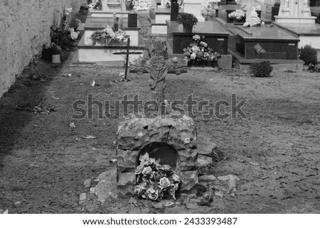 The photo  is a black and white image of a cemetery. There is a large cross in the center of the photo, with a smaller cross in front of it. There are flowers on either side of the cross, and 