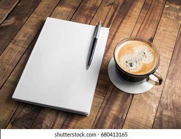 Photo Of Blank Closed Book, Pencil And Coffee Cup On Wooden Table Background. Responsive Design Mockup. Stationery Elements. Template For Placing Your Design.