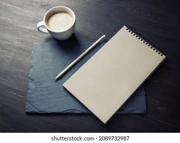 Photo of blank kraft notebook, pencil and coffee cup. Mockup for ID.
