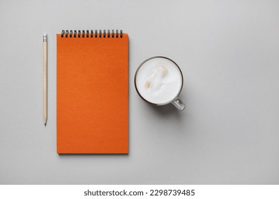 Photo of blank orange sketchbook, coffee cup and pencil on gray paper background. Flat lay.