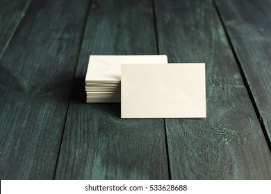 A photo of a blank white thick cardboard business card next to a pile of them, on a dark wooden background texture. A mockup or a minimalist banner with copyspace
