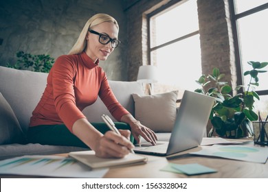 Photo of blond business lady texting notebook colleagues working home noticing startup details in organizer wear specs orange pullover sitting comfy sofa indoors
