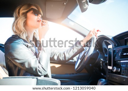 Photo of blonde in black glasses paints lips sitting in car