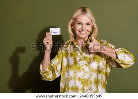 Photo of blonde hair mature age smiling grandmother promoting new ecard thumb up rate bank card isolated on khaki color background