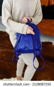 Photo Of A Blue Leather Backpack In Womens Hand. Girl Wearing Beige Sports Suit. Selective Focus