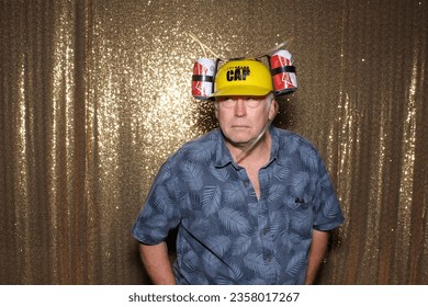 Photo Booth. Beer Hat. A man wears a BEER HAT while having his pictures taken in a Photo Booth at a party. Beer hats make it convenient to walk around hands free drinking beer. Booze Hats are Fun. 