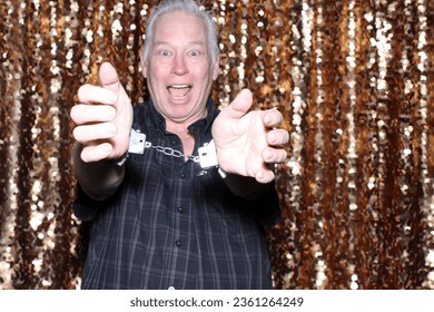Photo Booth. Hand Cuffs. A man smiles as he wears a set of Hand Cuffs. He just escaped from while waiting for his pictures to be taken in a Photo Booth. People world wide love Photo Booths. Handcuffs.