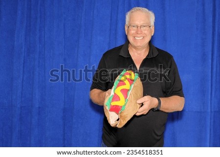 Photo Booth. Hot Dog costume for small dogs and cats. A man smiles as he holds a HOT DOG Costume for small dogs and cats while waiting for his picture to be taken in a Photo Booth. Hot Dog. Weiner dog