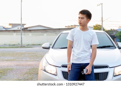 Photo of A boy iin white casual is chatting on his phone and leaning on the silver car hood. - Shutterstock ID 1310927447