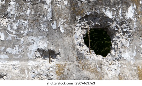 Photo of a broken cement wall or fence. Stone grunge odd wall with a hole. Damaged grungy crack and broken concrete wall