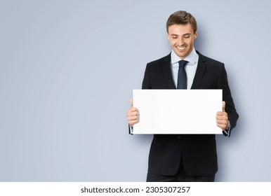 Photo of business man, employee, professional wear black confident suit, necktie. Businessman hold, show, demonstrate, advertise, promote empty white banner signboard. Isolated grey gray background - Powered by Shutterstock