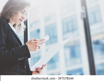 Photo business woman wearing suit, looking smartphone and holding documents in hands. Open space loft office. Panoramic windows background. Horizontal mockup. Film effect - Powered by Shutterstock