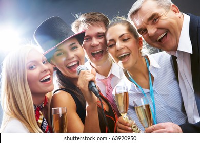Photo of businesspeople with flutes of sparkling champagne singing Christmas songs