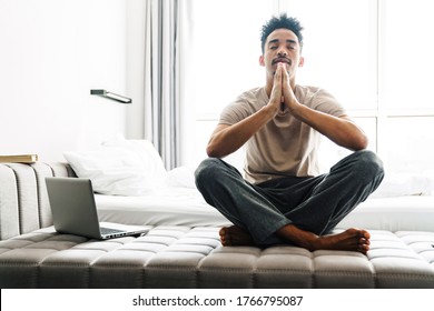 Photo of calm african american man with mustache meditating while sitting on sofa at bright room